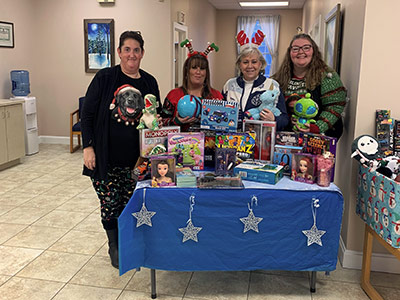 Four Women Wearing Christmas Sweaters Behind Toy Table