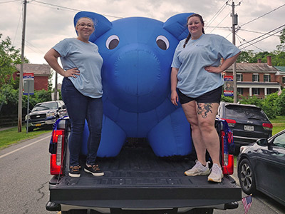 Autumn and Mykenzie standing in the back of a pickup truck with an inflatable piggy bank